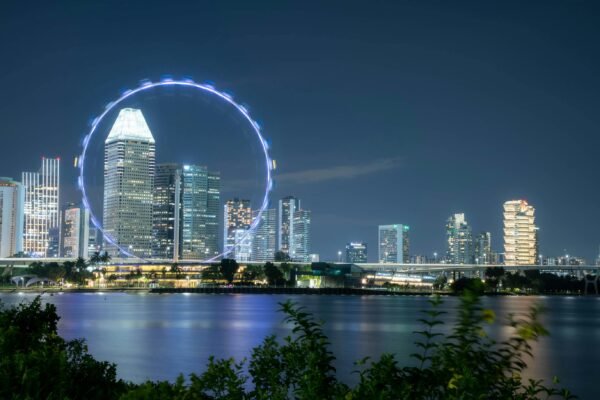 Beautiful night view of Singapore skyline with illuminated Ferris wheel and reflections on the river.